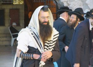 Ein Mann in traditioneller jüdischer Kleidung betet draußen zusammen mit anderen im Hintergrund.