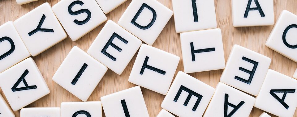 Scrabble-Buchstabensteine, die zufällig auf einer Holzoberfläche verstreut sind.