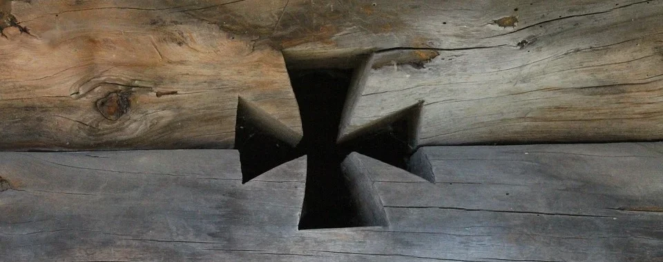 Ein schwarzes Malteserkreuz, aus alten Holzbrettern ausgeschnitten, mit strukturiertem, verwittertem Aussehen.