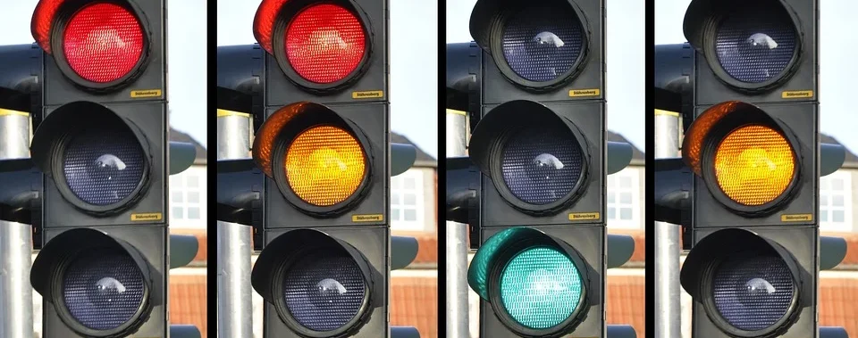 Vier Ampeln in Folge: Rot, Gelb, Rot und Gelb, Grün, vor unscharfem Hintergrund.