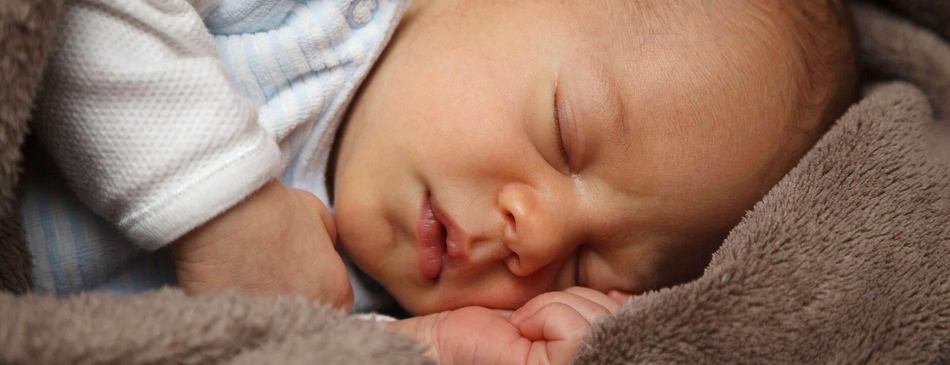 Eine Nahaufnahme von einem friedlich schlafenden Baby, eingekuschelt in eine weiche, braune Decken.
