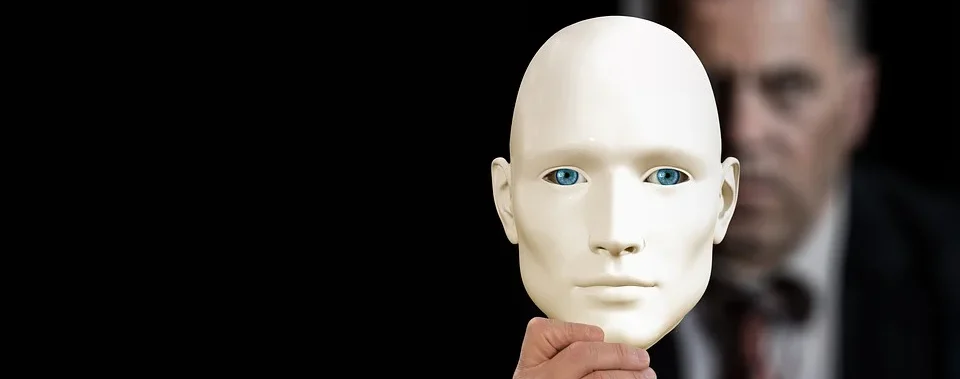Eine Hand hält eine weiße, ausdruckslose Maske mit blauen Augen, im Hintergrund eine verschwommene Gestalt.