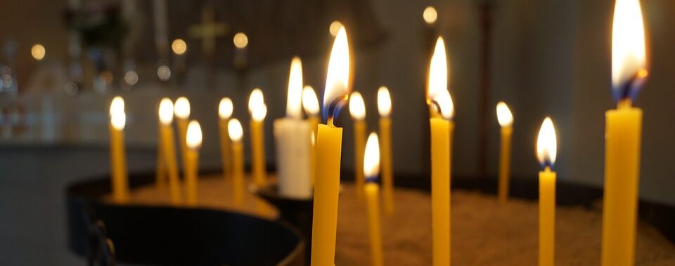 Mehrere gelbe Kerzen brennen in einem schwach beleuchteten Raum mit sanfter Hintergrundbeleuchtung und verschwommenen Objekten in der Ferne.