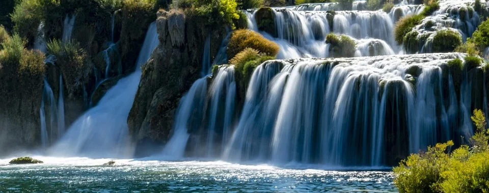 Ein üppiger, mehrstufiger Wasserfall ergießt sich in ein ruhiges, türkisfarbenes Becken, das von grüner Vegetation umgeben ist.
