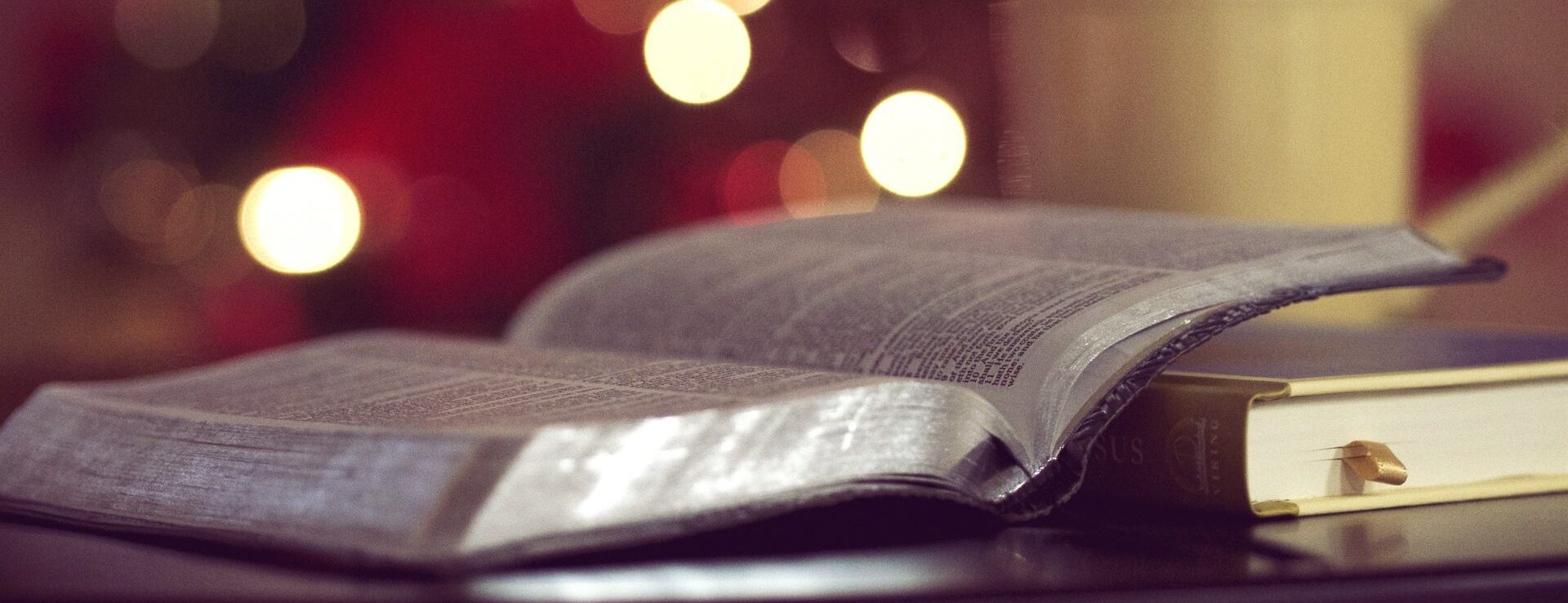 Eine offene Bibel mit verschwommenen Lichtern im Hintergrund, das eine warme, gemütliche Atmosphäre schafft.