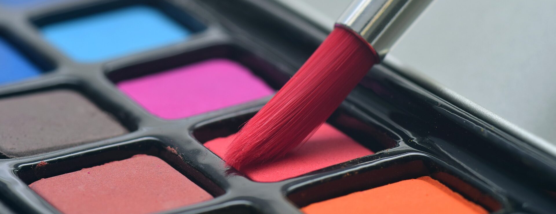 Nahaufnahme einer bunten Aquarellpalette mit einem in rote Farbe getauchten Pinsel.