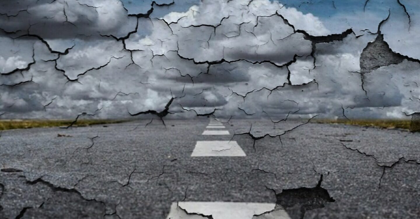 Eine rissige, abblätternde Textur überlagert einen bewölkten Himmel und eine verlassene Straße.