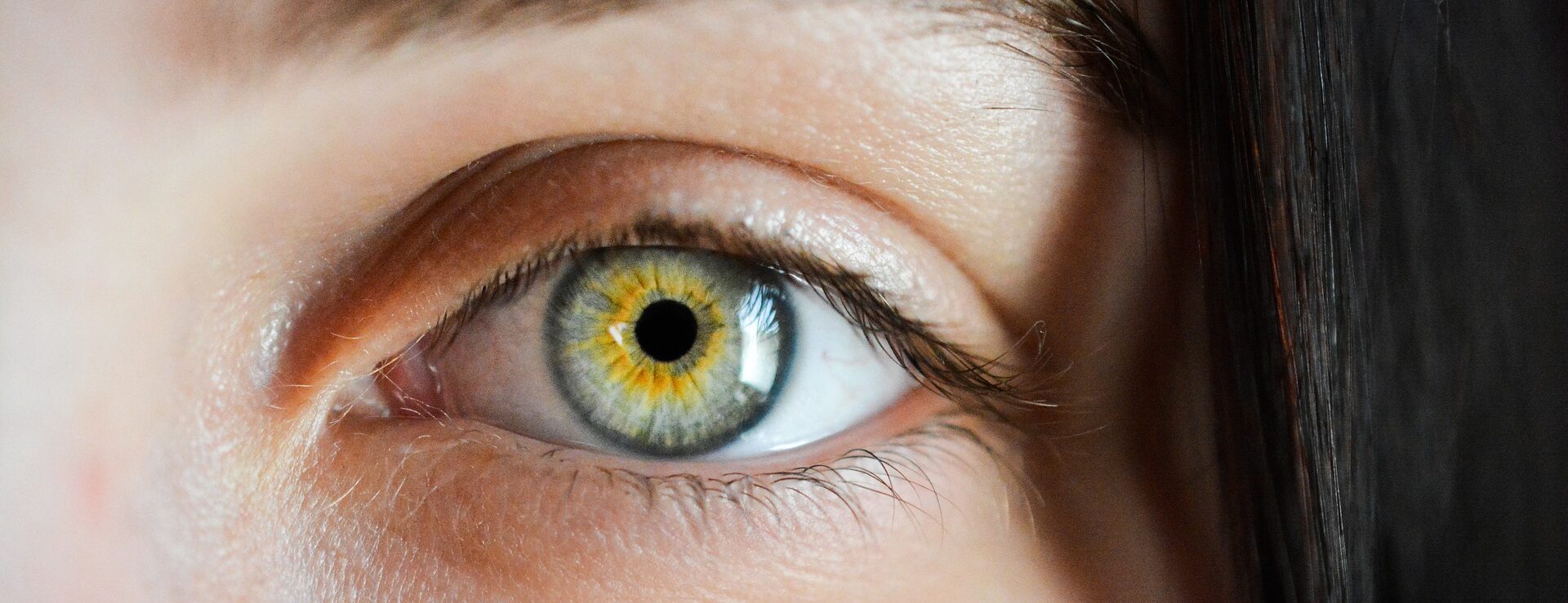 Eine Nahaufnahme eines menschlichen Auges mit grünen und gelben Farben in der Iris, umgeben von Wimpern.