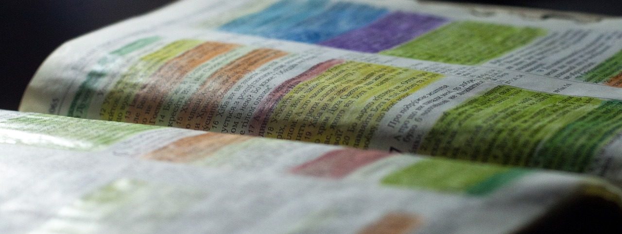 Offenes Buch mit hervorgehobenem Text in verschiedenen Farben auf einer dunklen Oberfläche.
