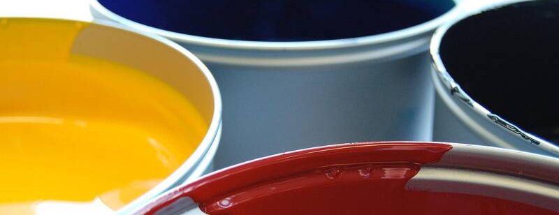 Vier geöffnete Farbdosen mit gelber, blauer, schwarzer und roter Farbe, aus der Nähe gezeigt.