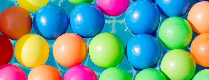 Bunte Plastikbälle schwimmen auf klarem, blauem Wasser und bilden ein lebendiges und verspieltes Muster.